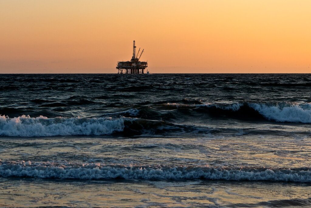 An oil rig sits out in the ocean as the sun sets.